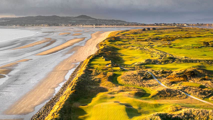 An aerial view of a golf course with sand dunes beside the sea