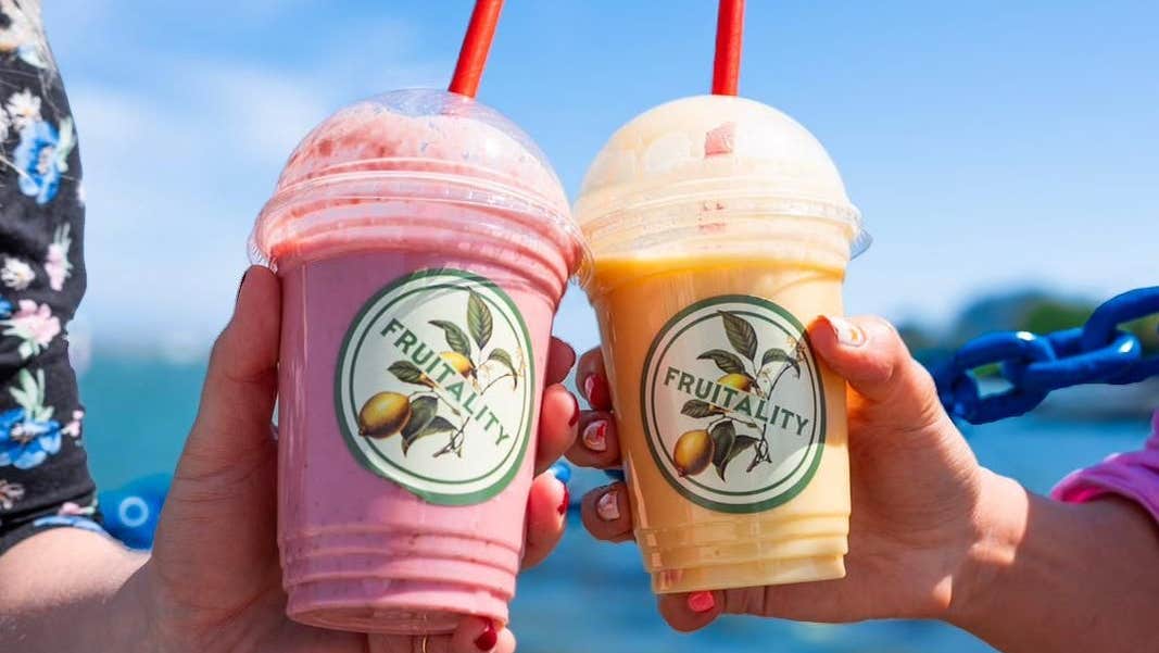 A close up of two people holding plastic cups with straws and colourful liquids