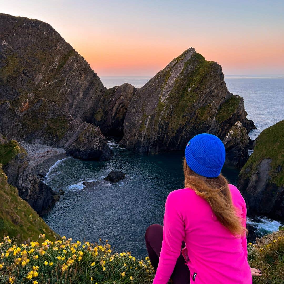 Woman looking out over cliffs at sunrise at Nohoval Cove in Cork.