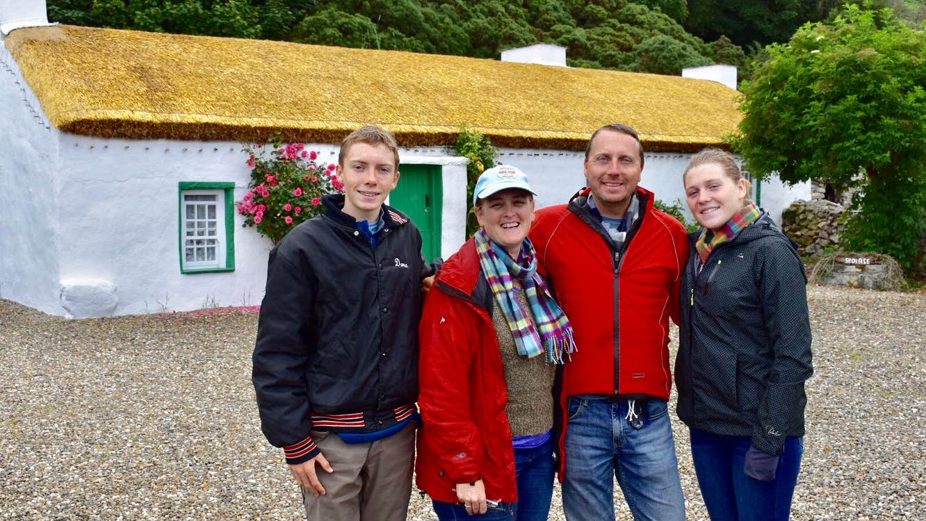 A family of four standing in front of a thatched cottage for a group photo