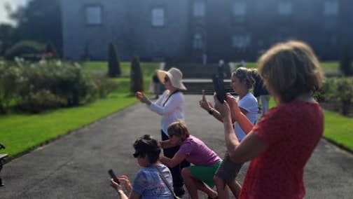 Kilkenny Leisure Phone Workshop, a group of people in gardens outside a castle, all pointing their phones in the same direction taking a photo.