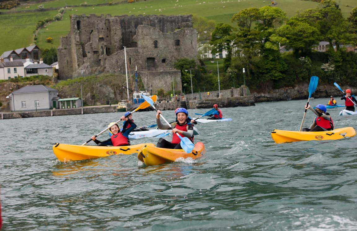 Kids kayaking in yellow kayaks in front of a castle in Louth