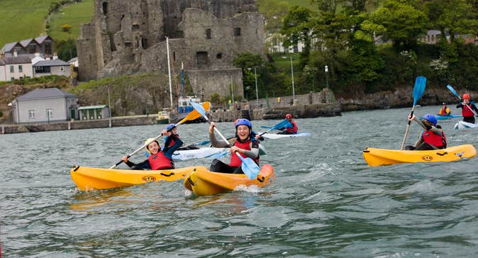 Kids kayaking in yellow kayaks in front of a castle in Louth