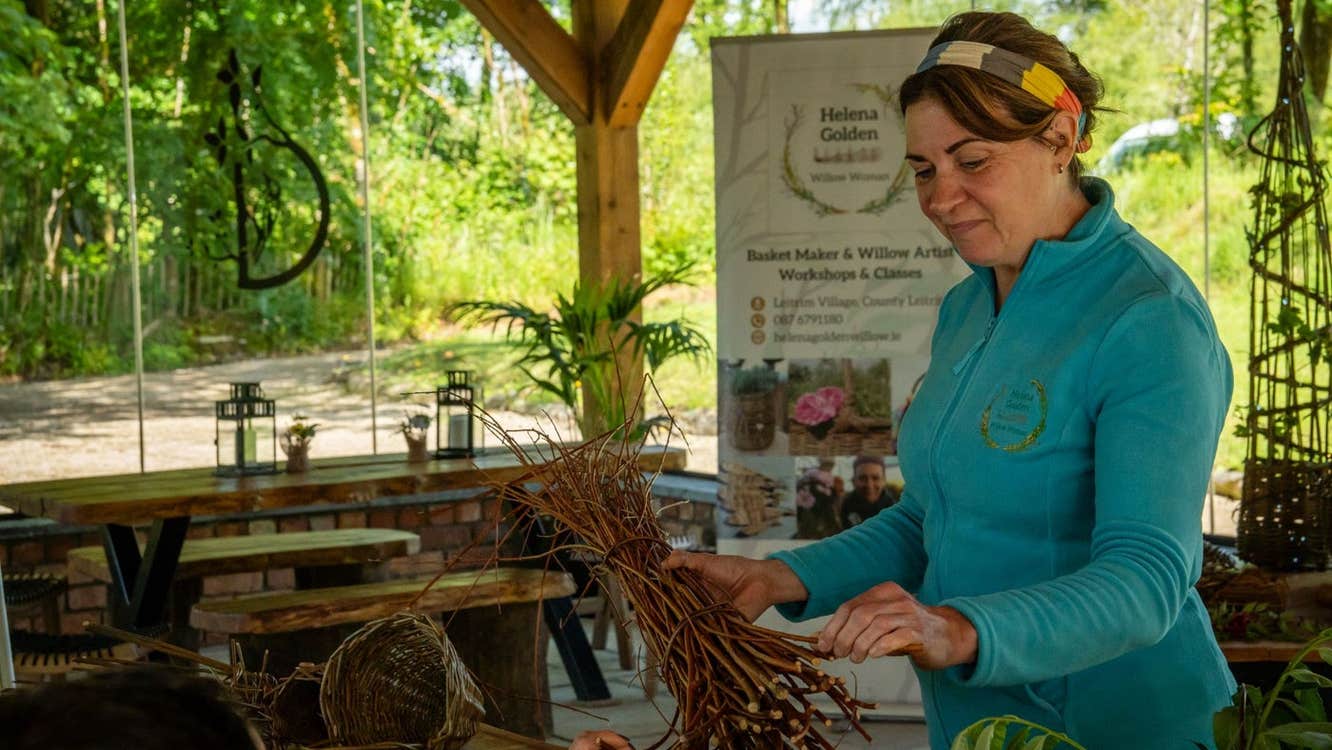 A lady holding a bunch of willow twigs in a workshop with views of trees from the windows