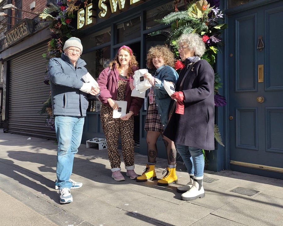 Four people standing outside a pub posing with small branded bags with food on them