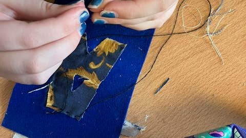 Someone is a creating an artwork by sewing a piece of fabric onto something.