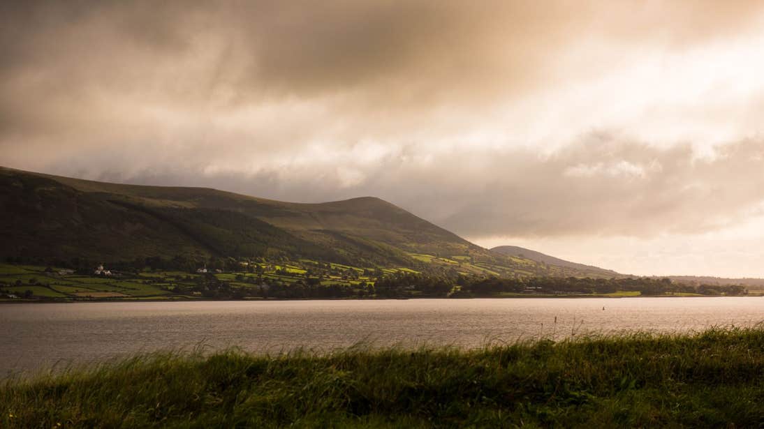 A peaceful Carlingford Lough with a backdrop of green fields and mountains