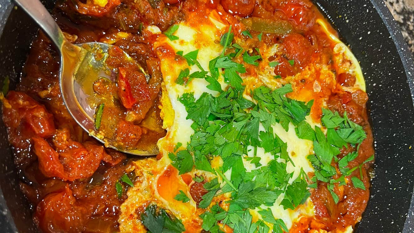 A pot with tomatoes and pasta mixed with a sauce sprinkled with green leaves