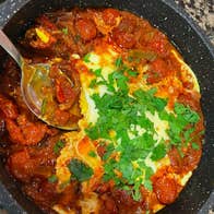 A pot with tomatoes and pasta mixed with a sauce sprinkled with green leaves