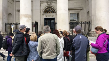 A group of people and a tour guide standing outside a stately building on a city street