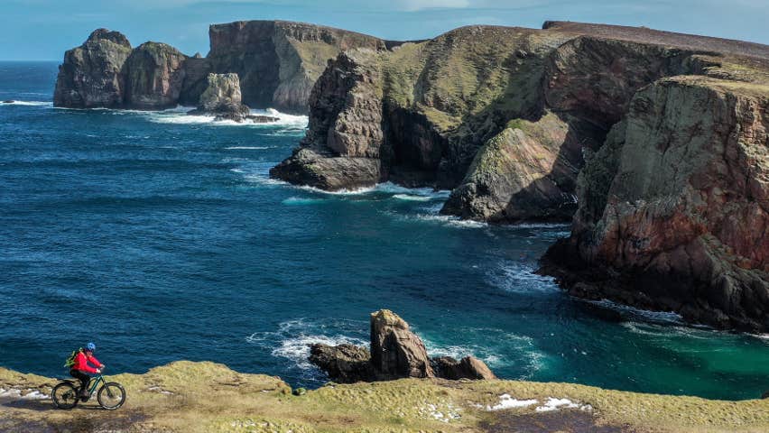 A cyclist rides past cliffs and sea views
