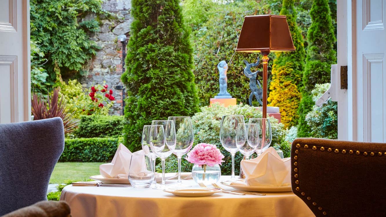 A set table with wine glasses next to a window overlooking a garden