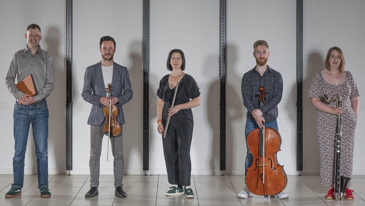 A line of 5 musicians with their instruments, standing slightly apart.