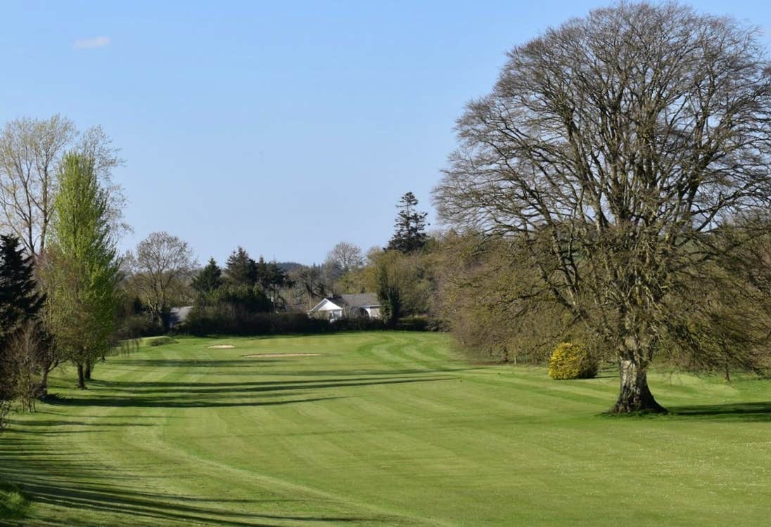 Golf green with trees on either side and a white house in the background
