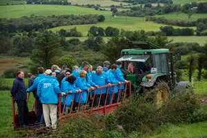 A tour group standing on trailer with a tractor as they enjoy a West Cork Farm Tour.