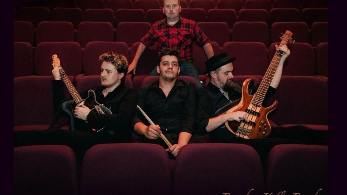 A group of 4 men with musical instruments seated in empty theatre seats