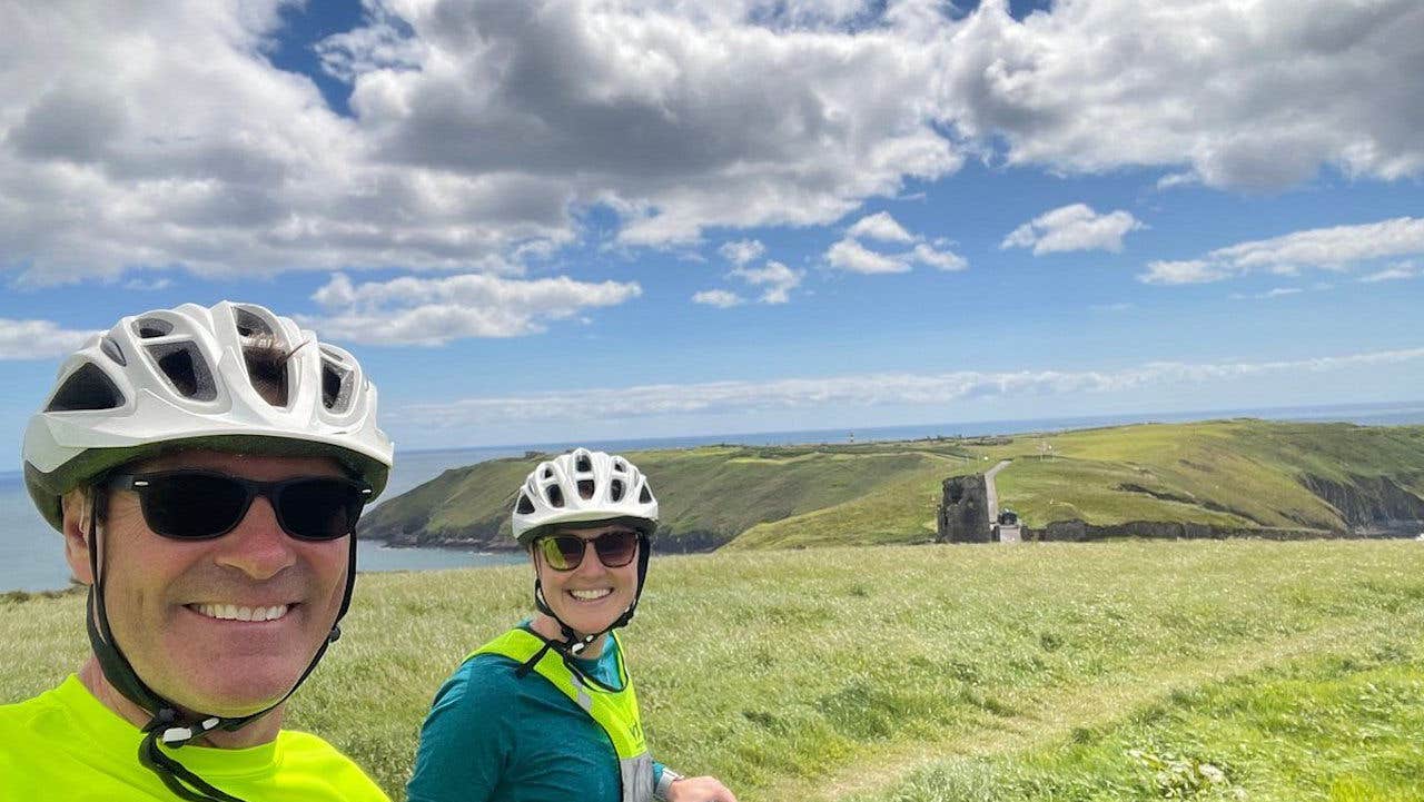Two cyclists with helmets on and coastal view in background