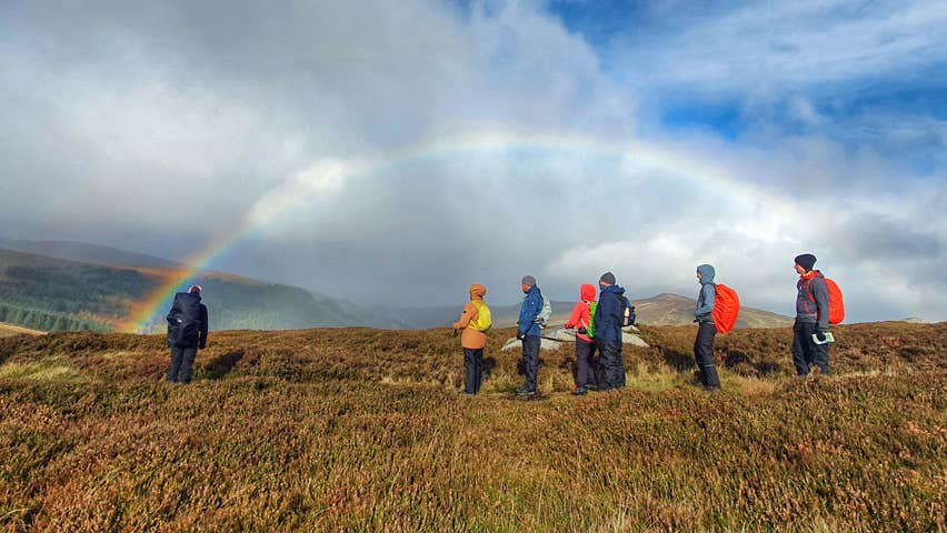 A group of walkers with the arc of a rainbow captured behind them in the distance