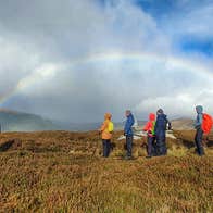 A group of walkers with the arc of a rainbow captured behind them in the distance