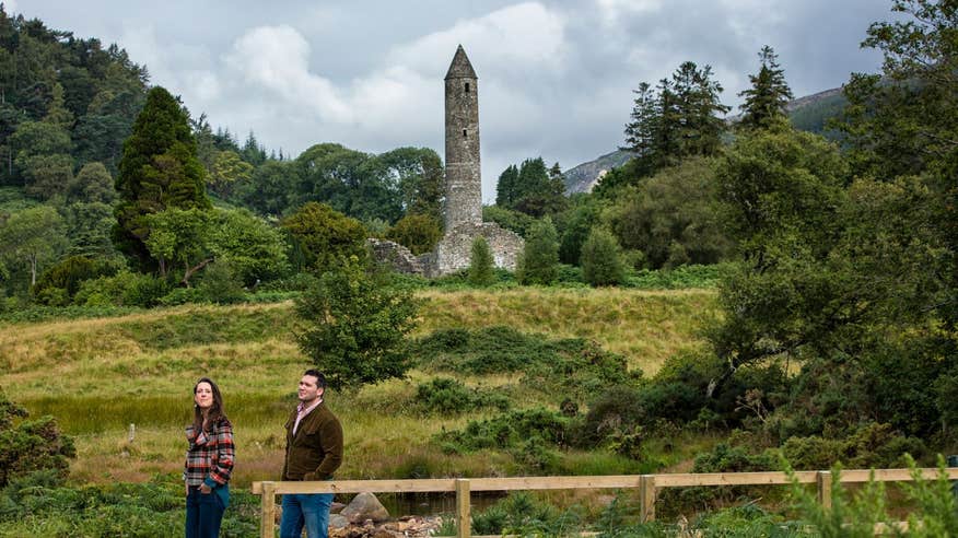 People walking past a round tower in Glendalough, Wicklow