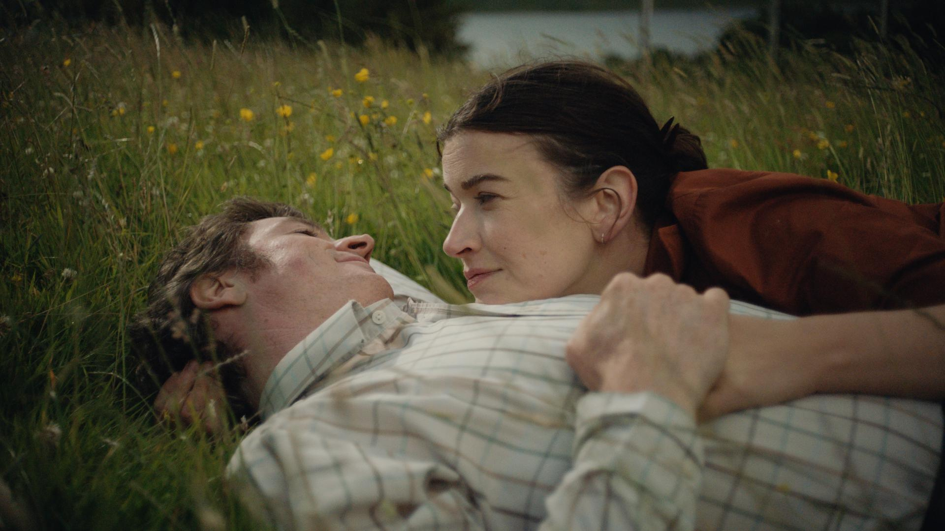A man and a woman are lying next to each other in field.