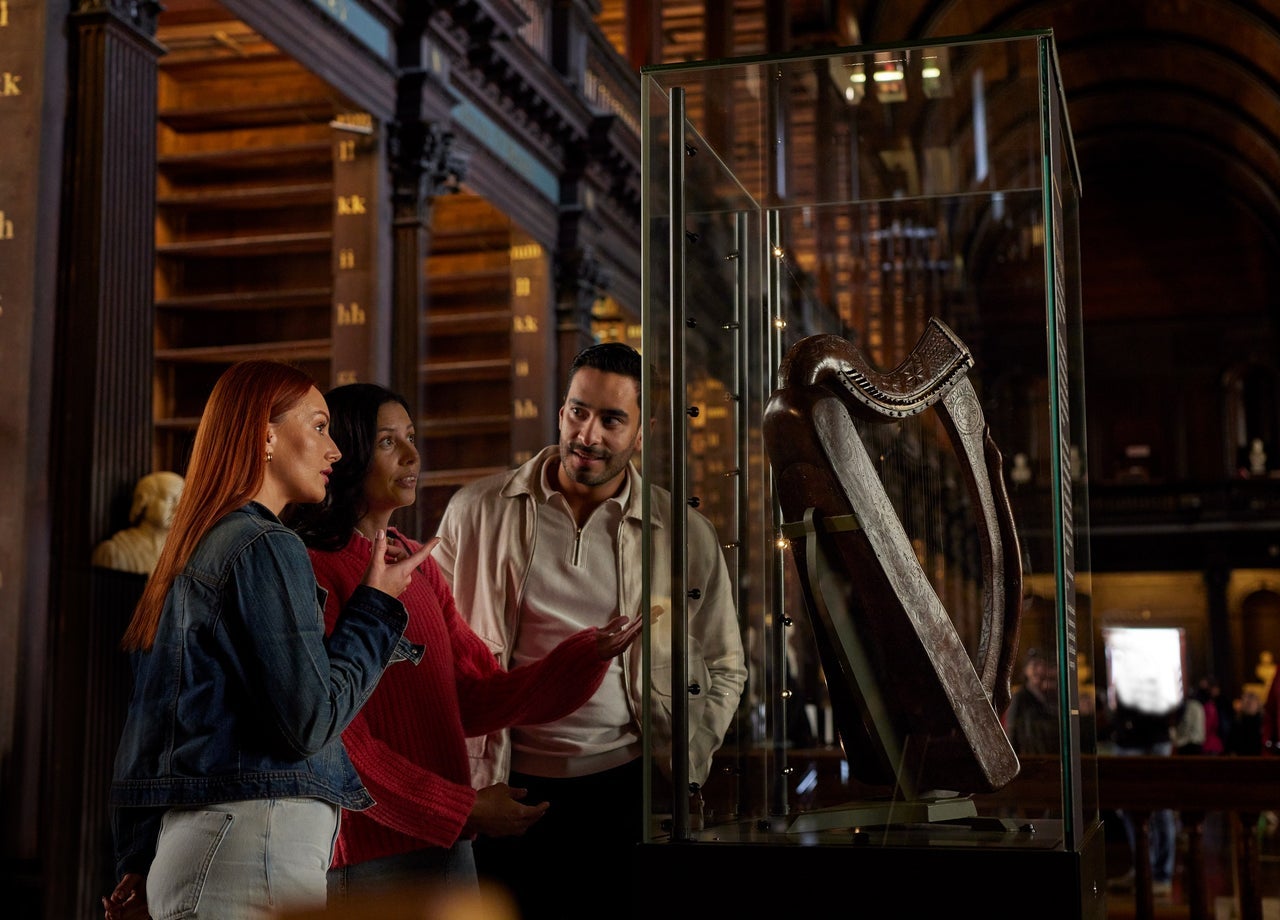 Three people looking at a wooden harp in a glass display case