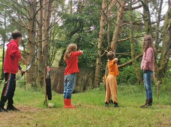 Axe Club showing four children practicing archery in a forest setting