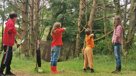 Axe Club showing four children practicing archery in a forest setting