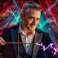 A smiling man in suit and shirt is holding a magic wand with bright coming out in a wiggly line.