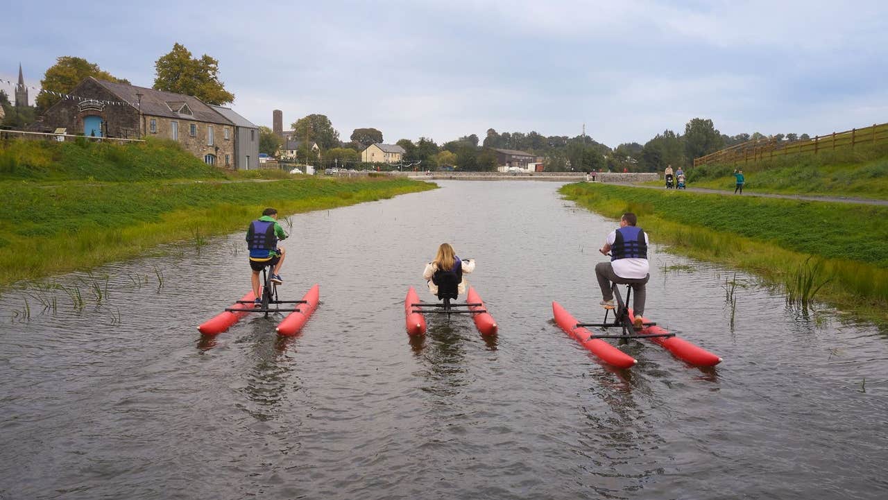 Three people cycling water bikes on a canal