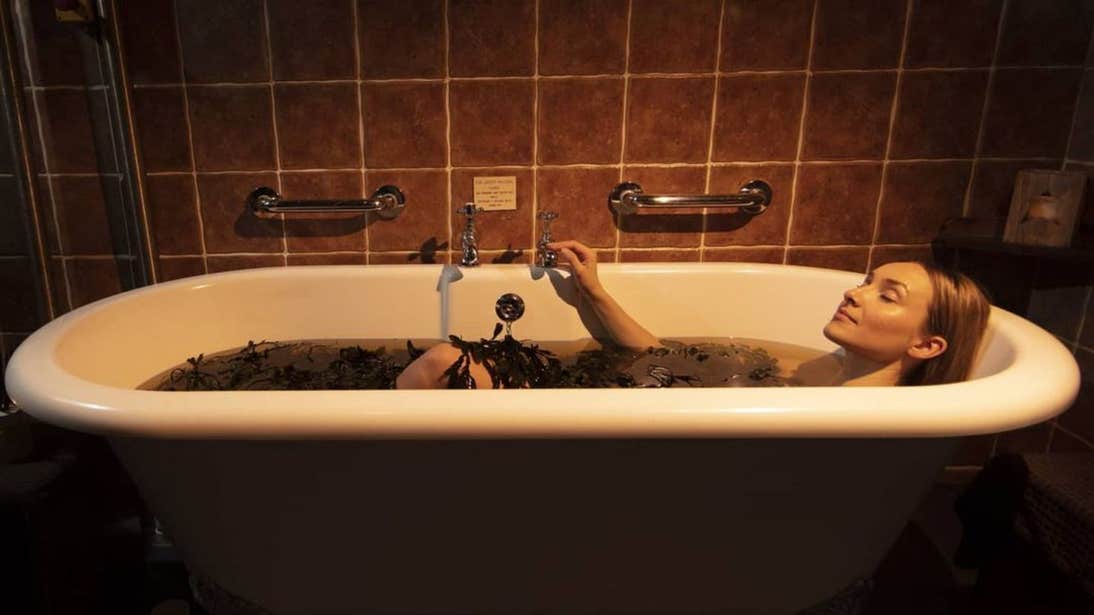 A woman relaxing in a seaweed bath in a dimly lit room.