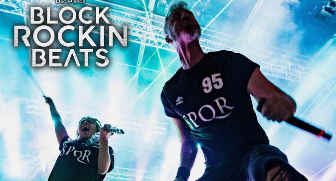 Dec Pierce Block Rockin Beats. 2 men in dark T-shirts on a stage with bright lights behind.
