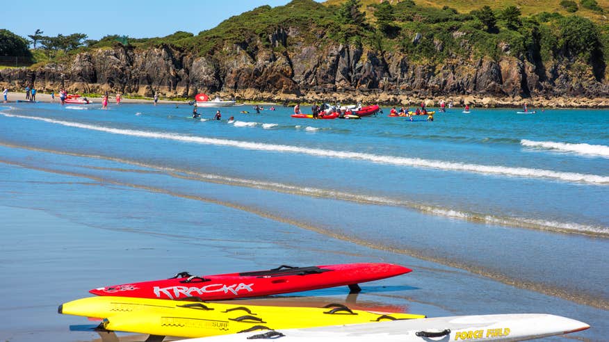 Surfboards lying on the shore with people playing in the sea against a backdrop of mountains at Marble Hill Beach, Donegal