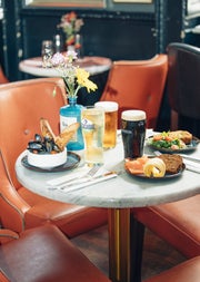 Three pints and three plates of seafood on a marble table with leather chairs