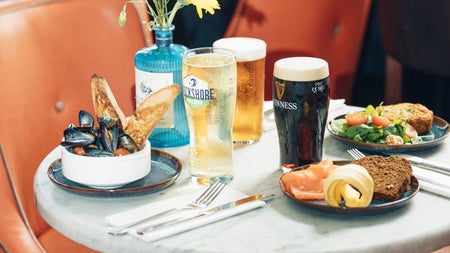 Three pints and three plates of seafood on a marble table with leather chairs