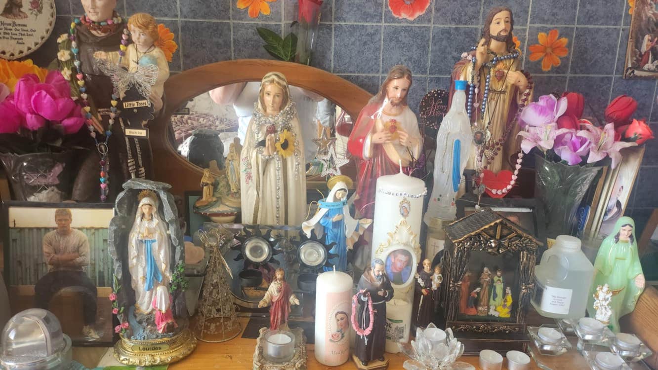 Various religious statues, candles and beads are on a table.