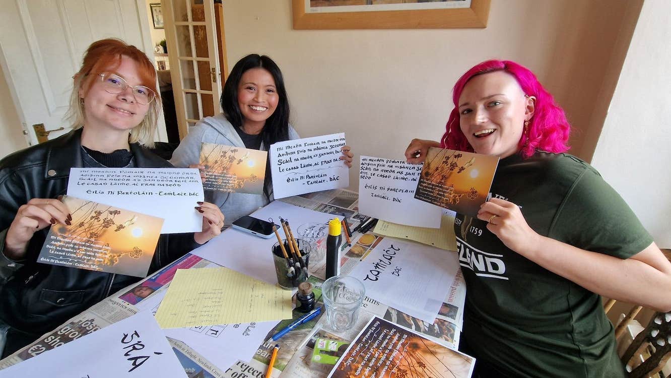Three girls holding up cards with Irish calligraphy on them