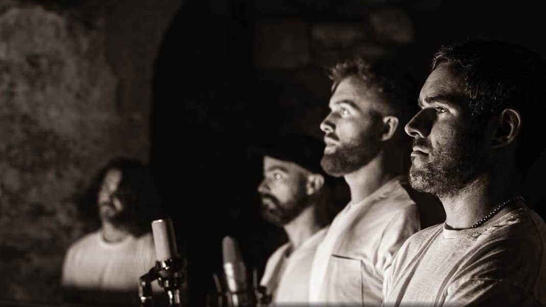 Black and grey shot of 4 men in a line, viewed from the side, fading to blurry in the distance, dark background.