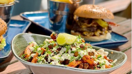Burger and dressed fries meal with drinks on a table at an outdoor dining area