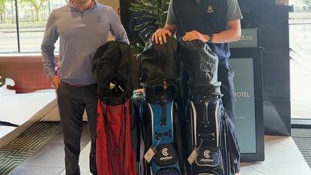 Two people with three golf club bags standing in a hotel lobby