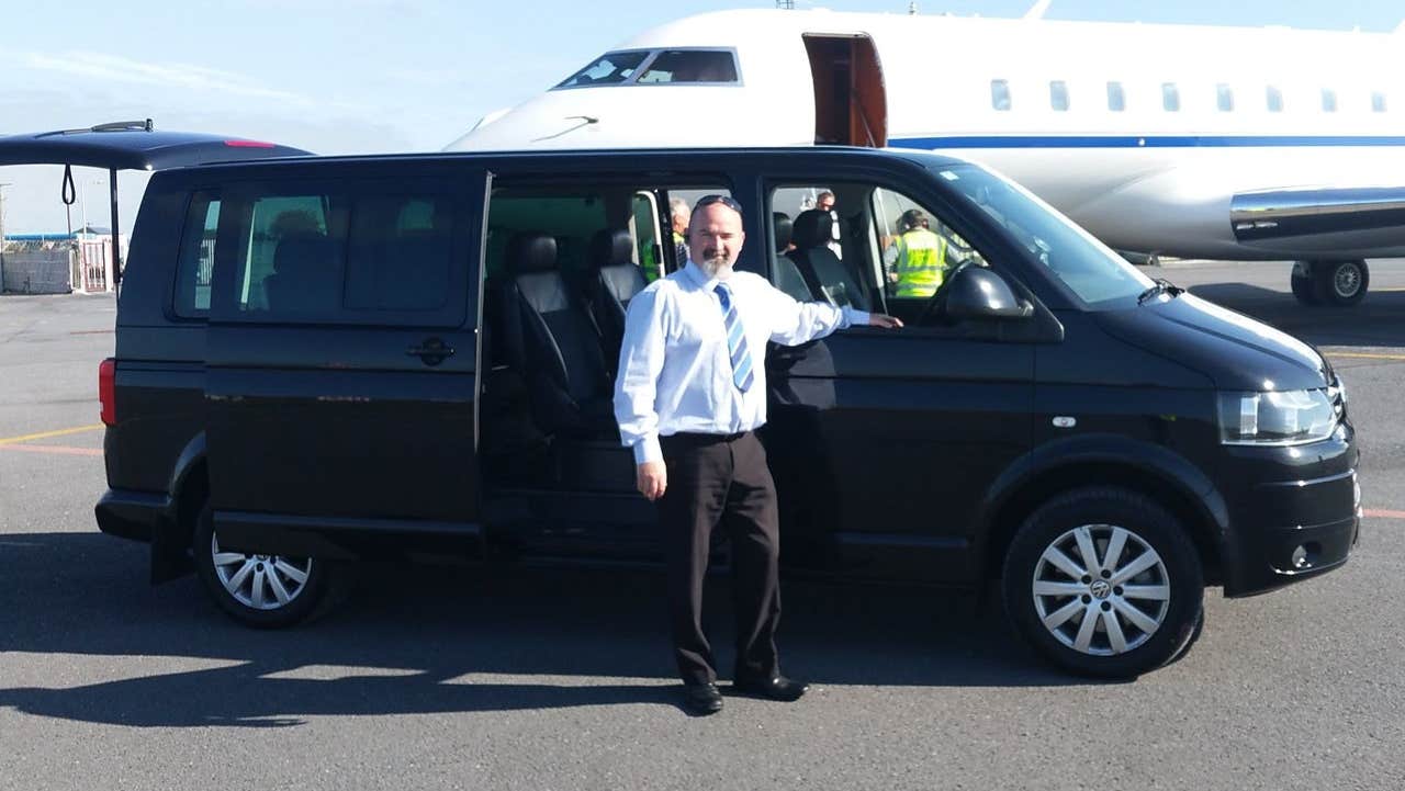A driver standing at his van with an airplane in the background