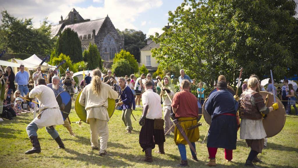 Battle re-enactment in a grassy area on a sunny day with people looking on.