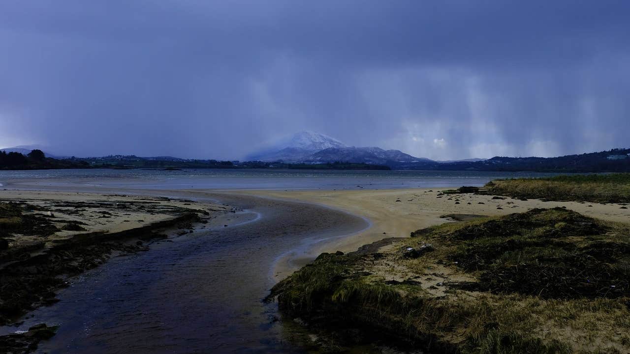 A coastal view with a mountain in the distance under a moody sky
