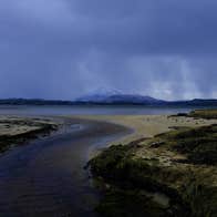 A coastal view with a mountain in the distance under a moody sky