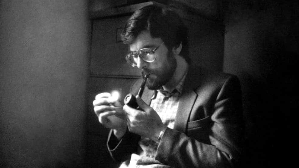 Black and white image of a seated man lighting a pipe.