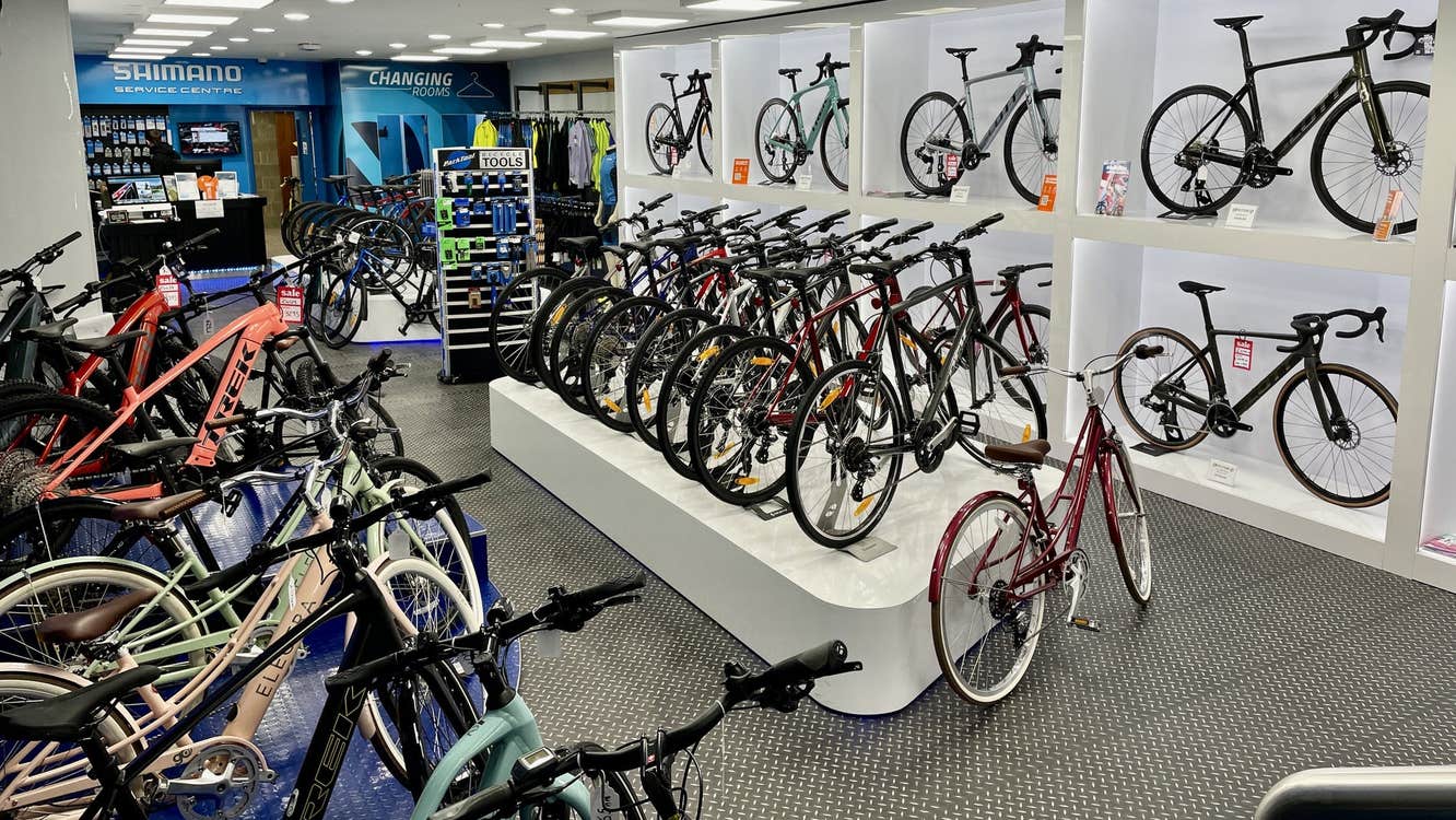 Rows of mountain bikes on display on a grey shop floor with with shelves to the right