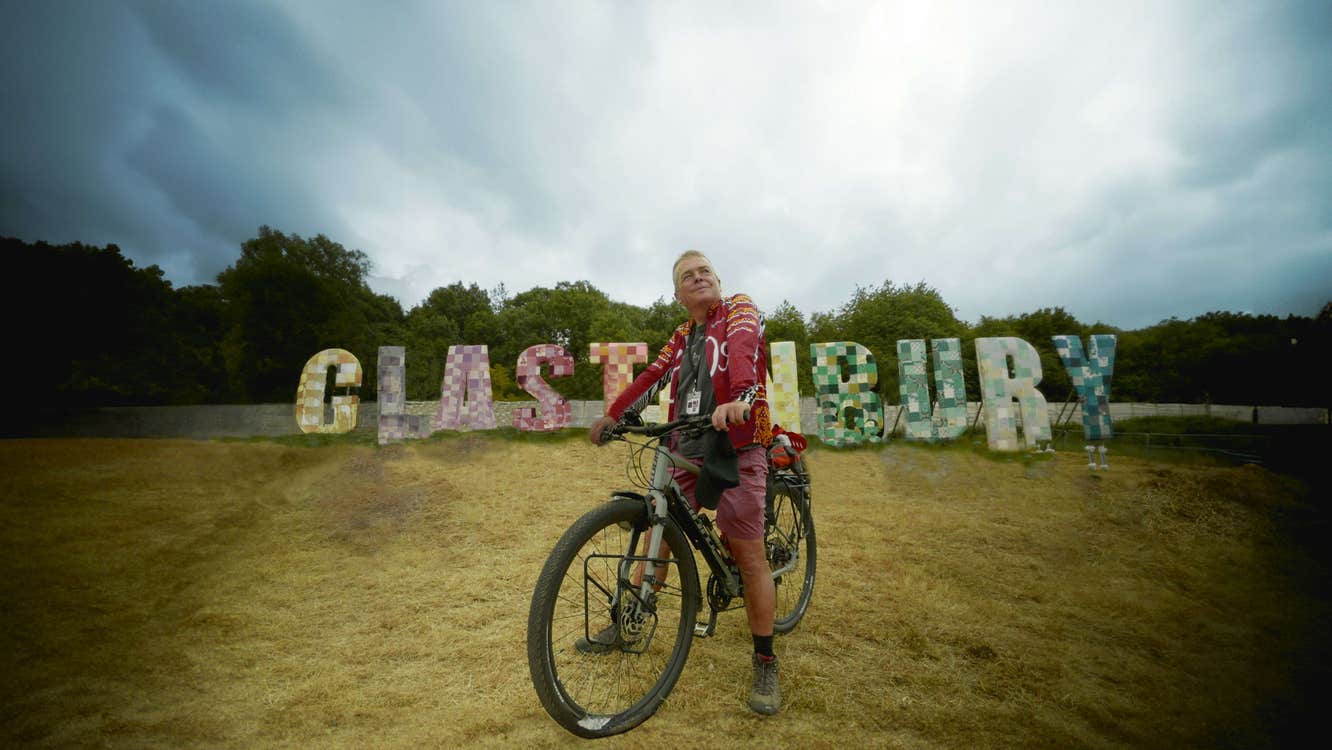 A man on a bicycle in front of letters that spell "Glastonbury".