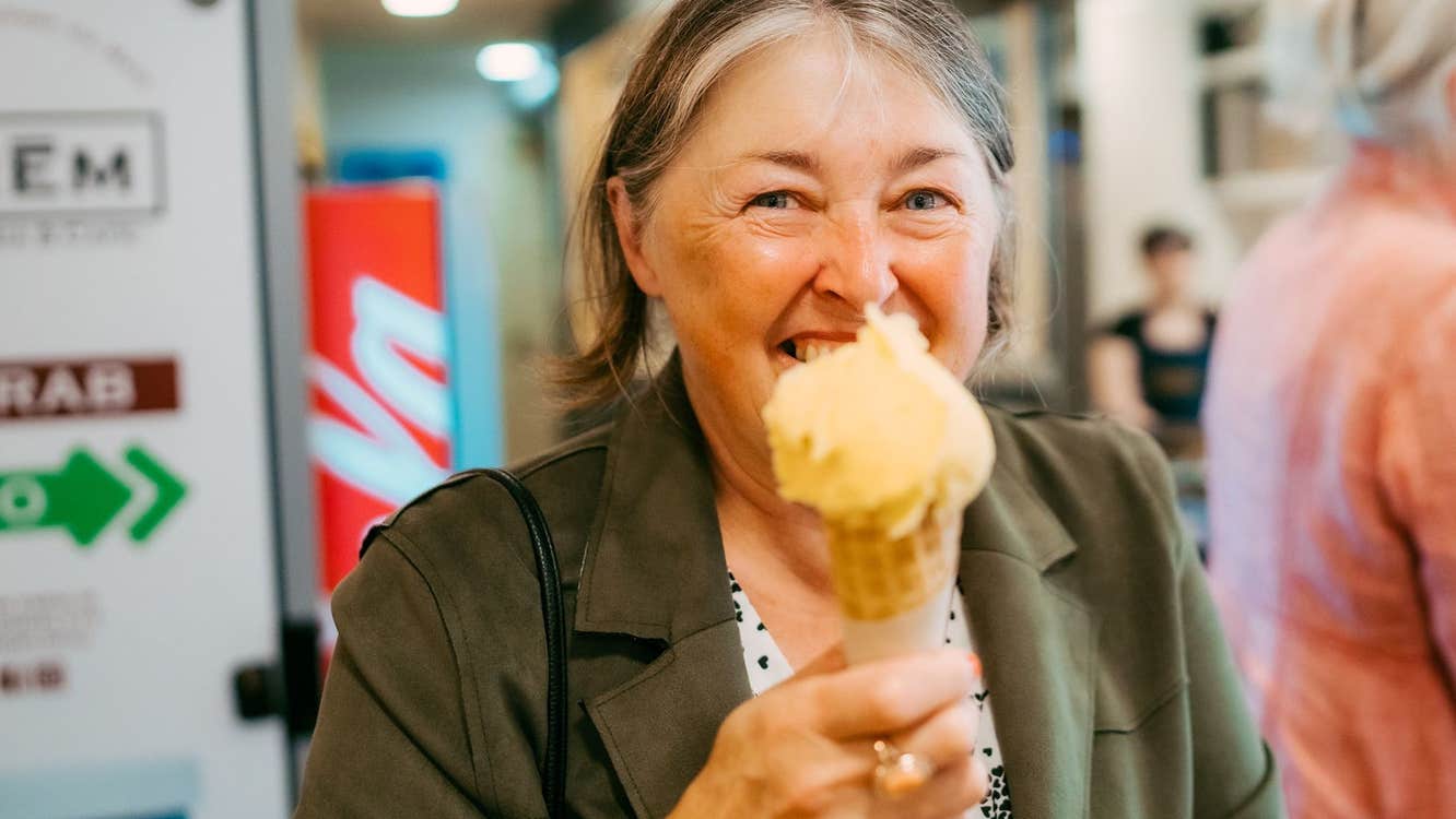 Lady holding an ice cream and cone while smiling at the camera