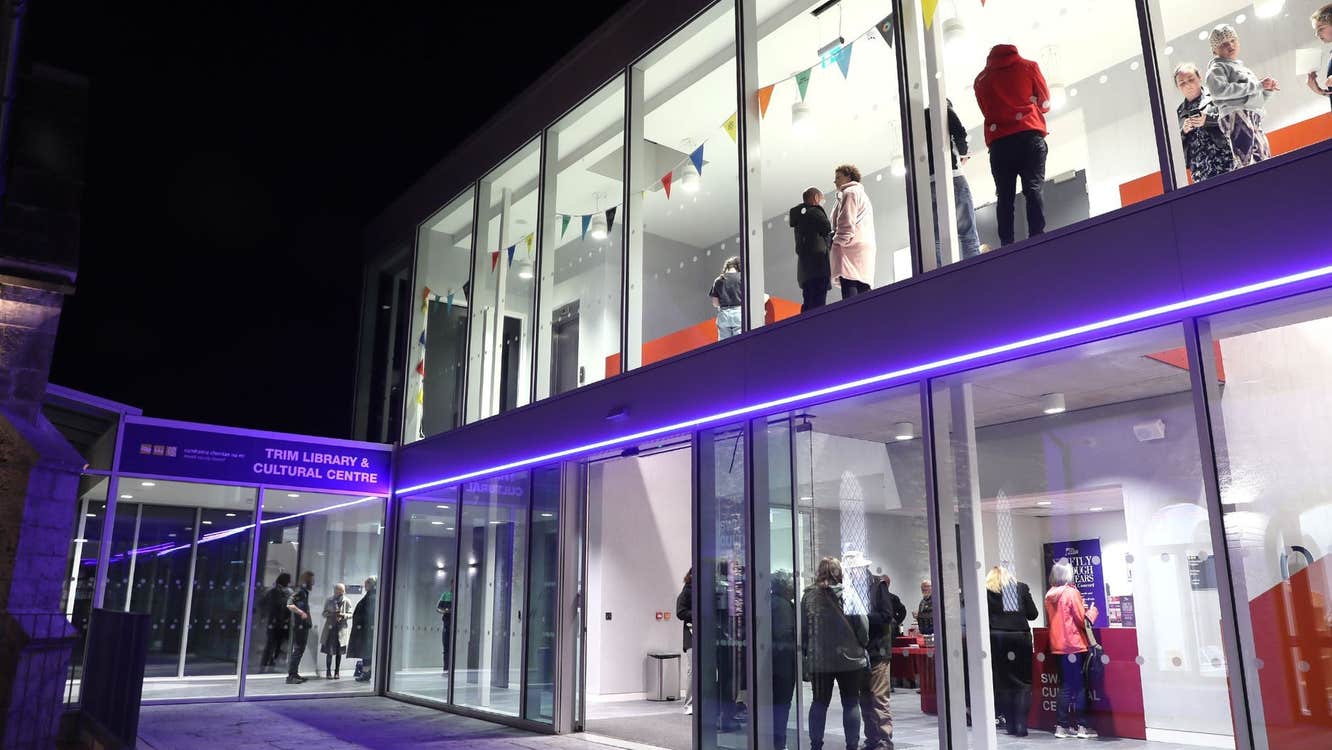 The exterior of the Swift Cultural Centre at night with people inside a well lit lobby and waiting area