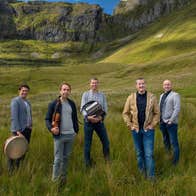 Group of 5 men standing in grassy area with backdrop of rocky hills